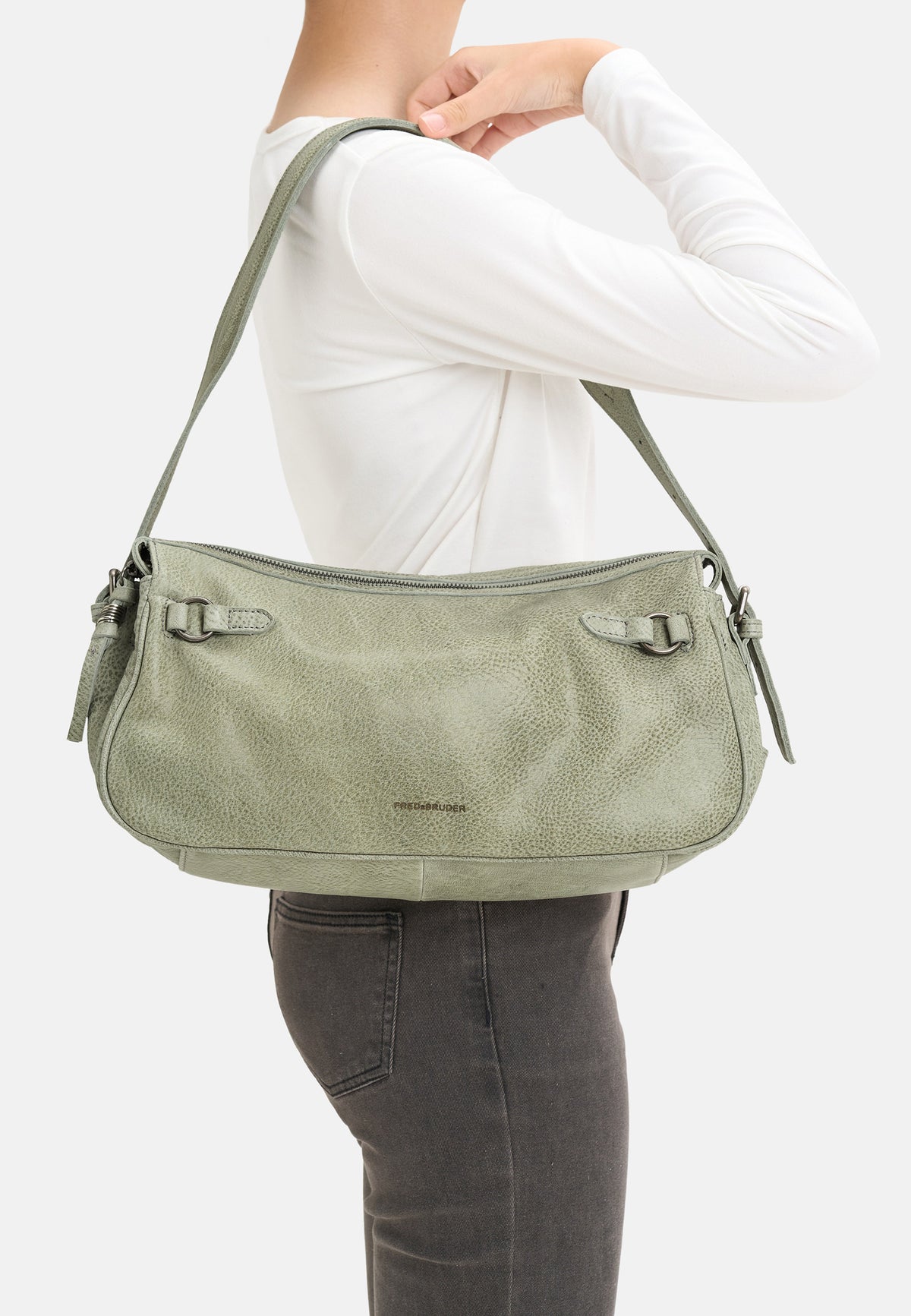 Hellgrüne Schultertasche seitlich getragen, mit Schnallenverschluss und Quasten.