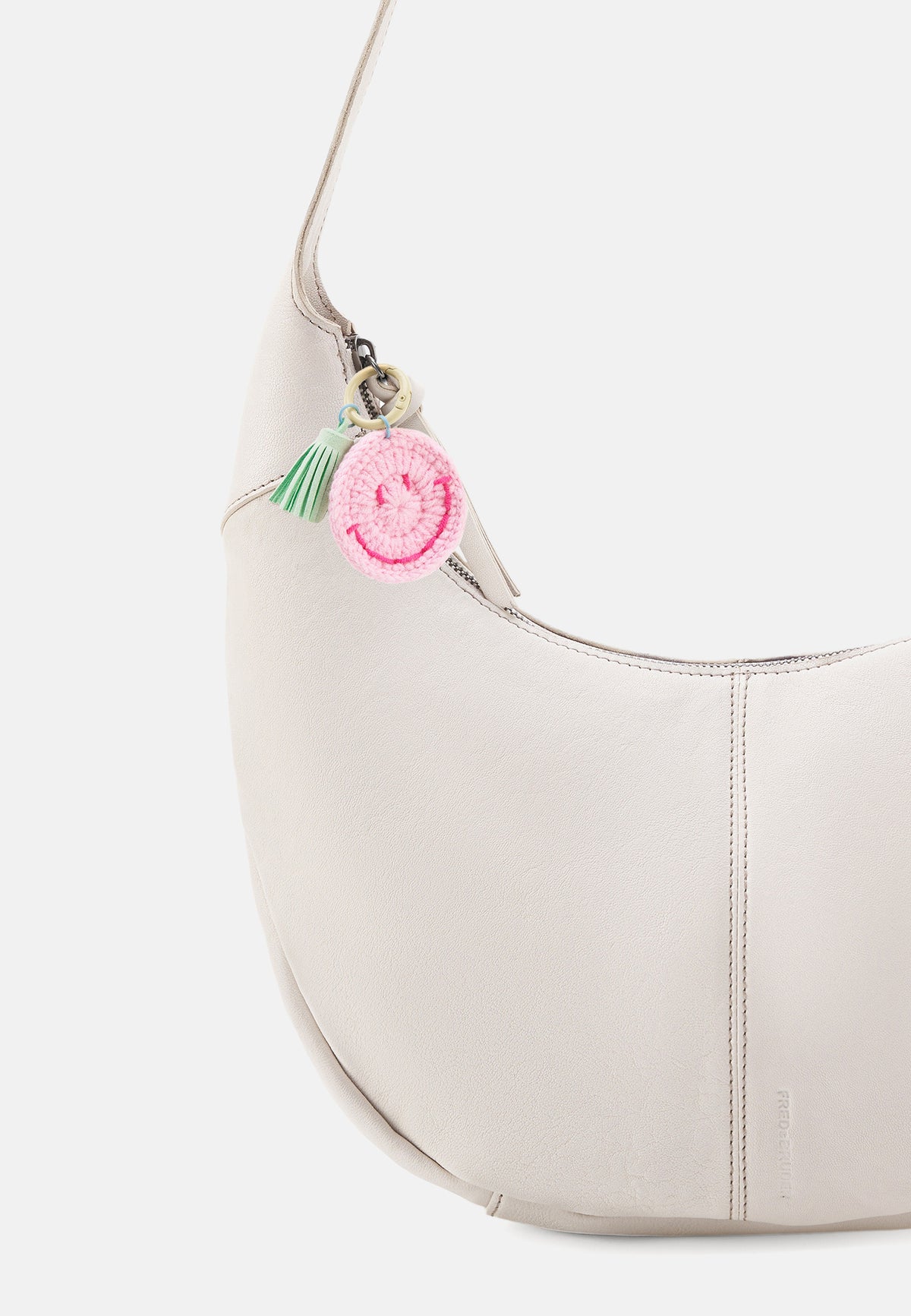 Cremefarbene Hobo-Tasche mit rundem pinkem Anhänger und grünen Fransen